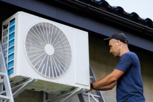 A man on a ladder performing air conditioning service on an outdoor AC unit in El Paso.